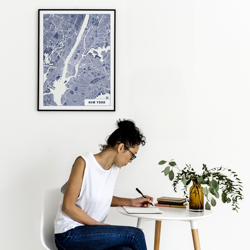 Poster du plan de New York bleu et blanc, dans un cadre noir sur un mur blanc au-dessus d’une petite table ronde