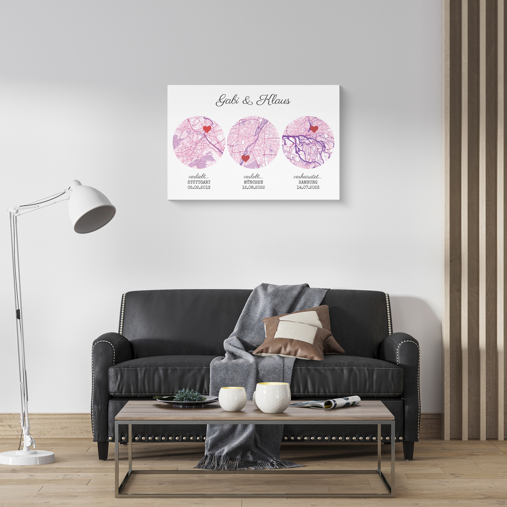 Poster mit drei runden Stadtkarten in Rosa, Namen und Beziehungsdaten über einem dunklen Sofa im Wohnzimmer