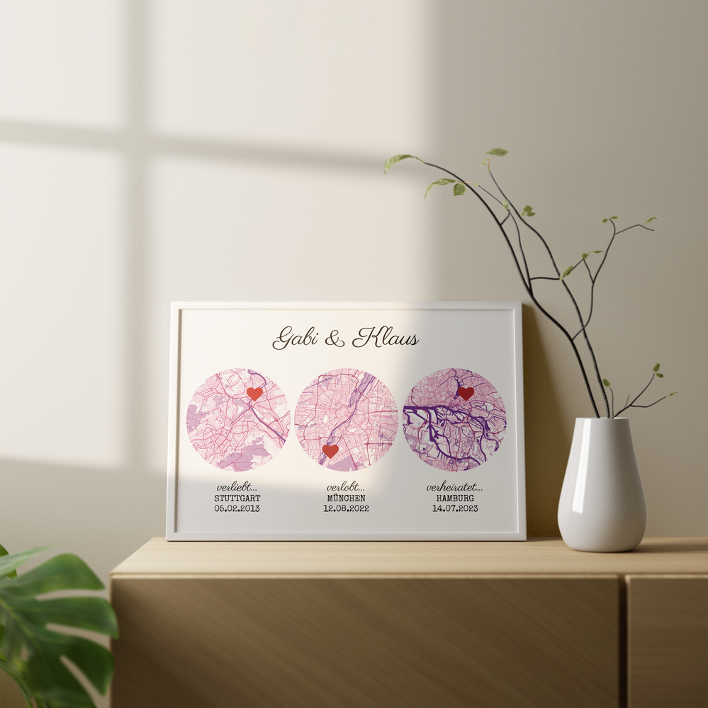Drei rosa Stadtkarten im weißen Rahmen auf einer Holzkommode neben einer Vase als Geschenkidee fürs Brautpaar