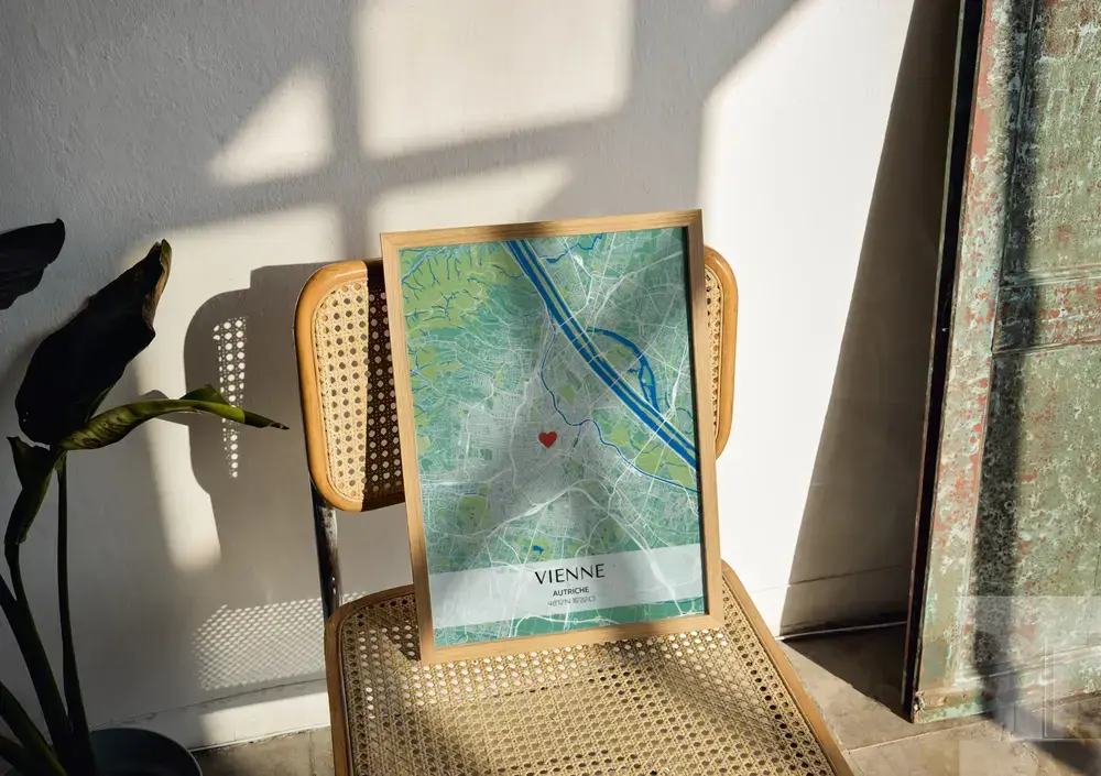 Affiche de plan de ville vert et bleu avec coordonnées, encadrée en bois naturel sur une chaise cannée au soleil