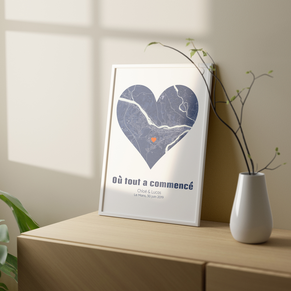 Affiche de plan de ville en forme de cœur, dans un cadre blanc posé sur un meuble en bois près d’un vase